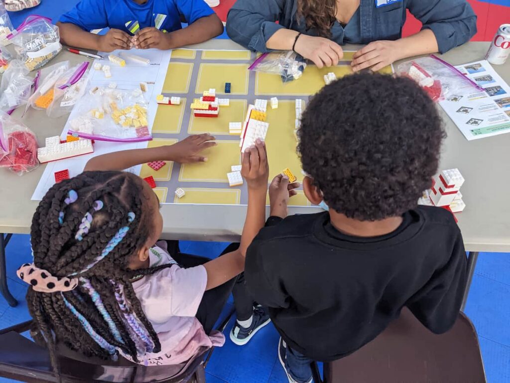 Three children and one woman use Lego pieces at a table.