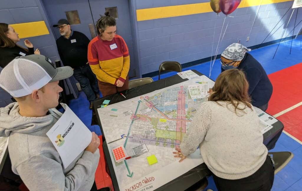 Four people gathered around a table, looking at a Jackson Ward Community Plan map and document