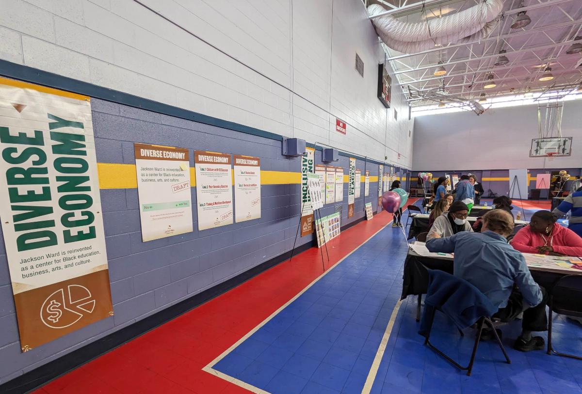 Posters on a wall, alongside people sitting at tables.