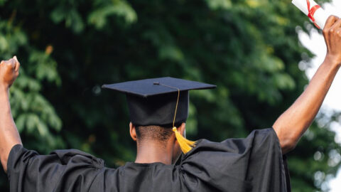 A student cheering in a graduation robe and hat, holding a diploma